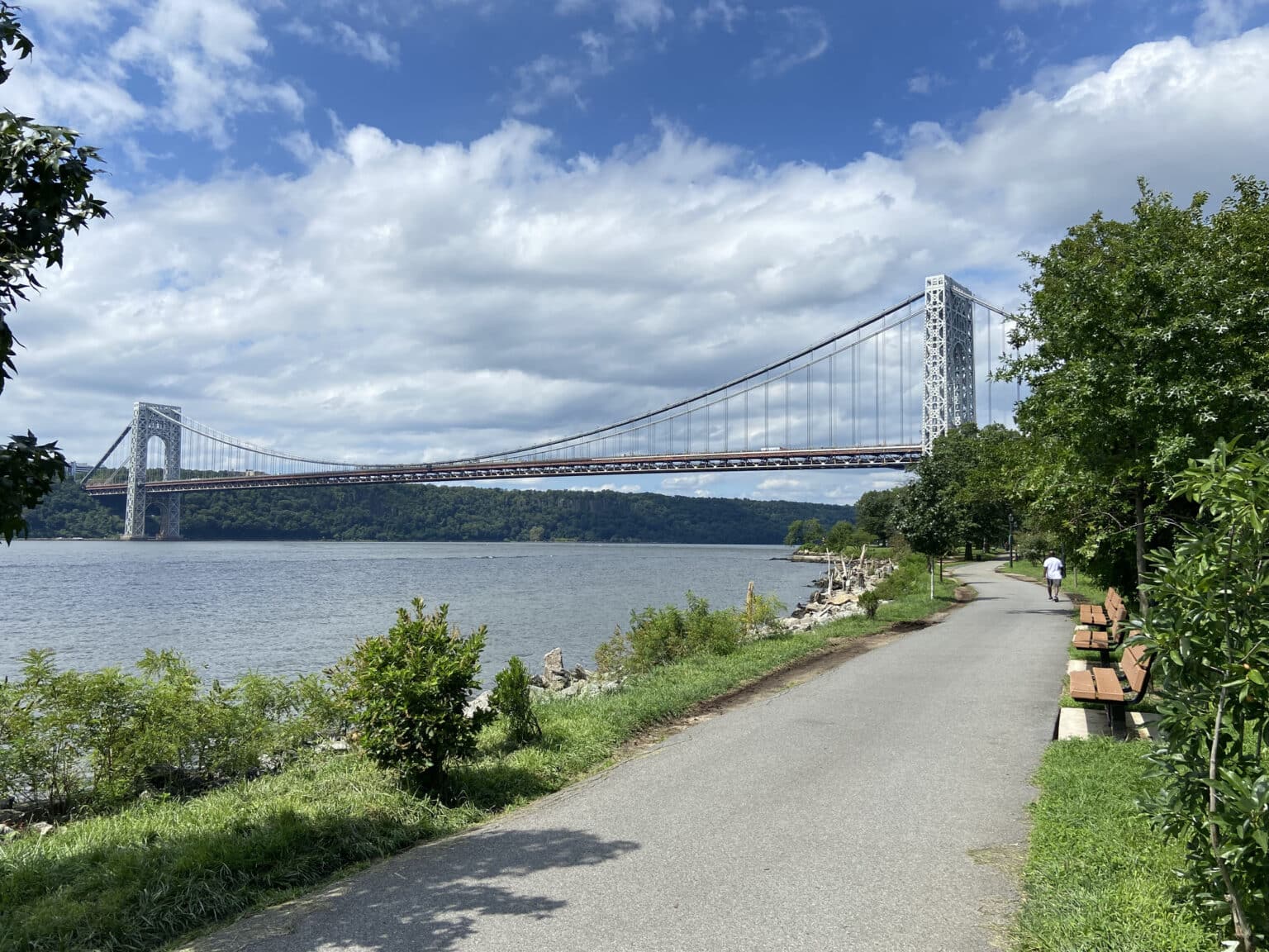 View of the Manhattan Waterfront Greenway curving next to the Hudson River and the George Washington Bridge in the background on a summer day in Riverside Park, New York City