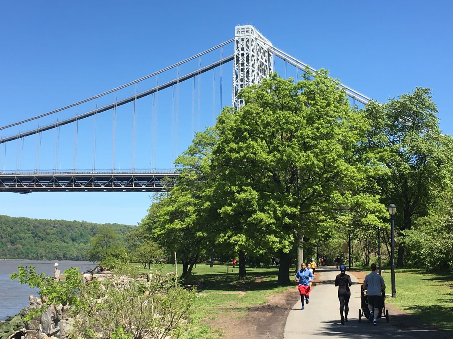People exercising on the Manhattan Waterfront Greenway in Riverside Park with views of the George Washington Bridge on a sunny day in New York City
